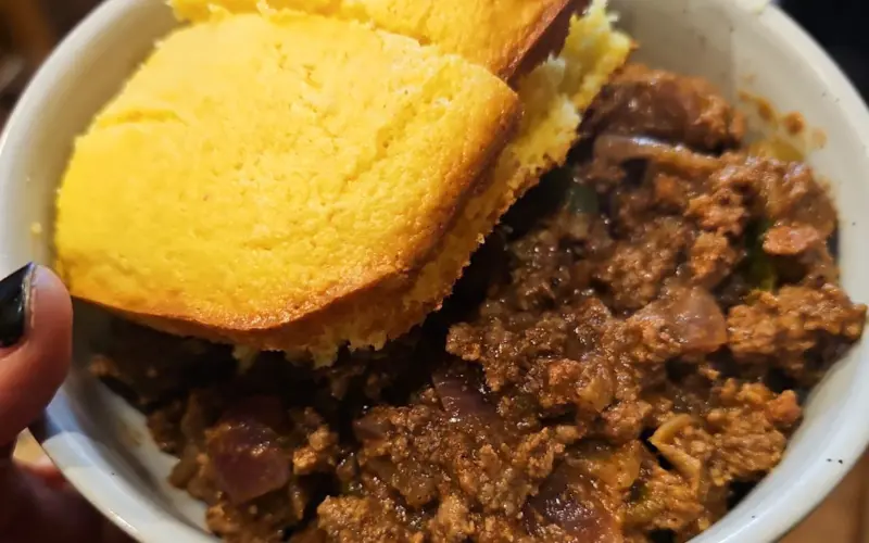 This image shows a bowl full of venison chili with cornbread on the side.